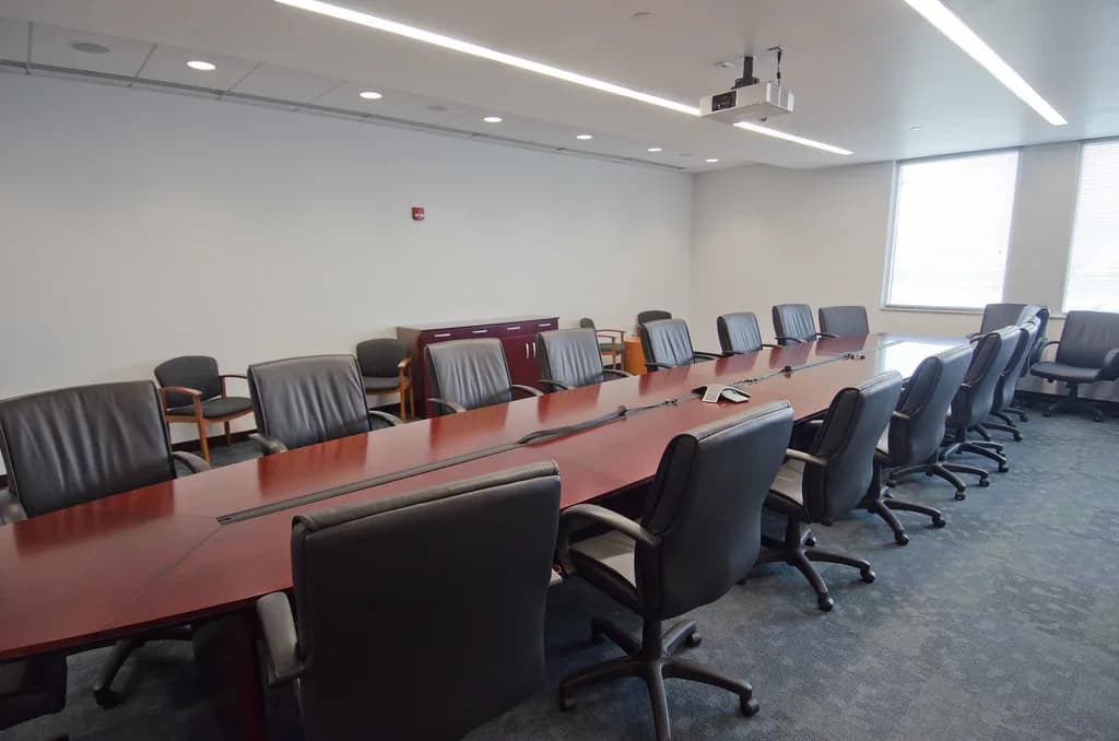 An empty boardroom: a long table, leather chairs and a projector overhead.