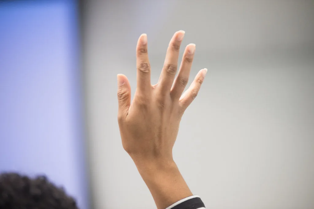 A hand raised to ask a question in a meeting room.