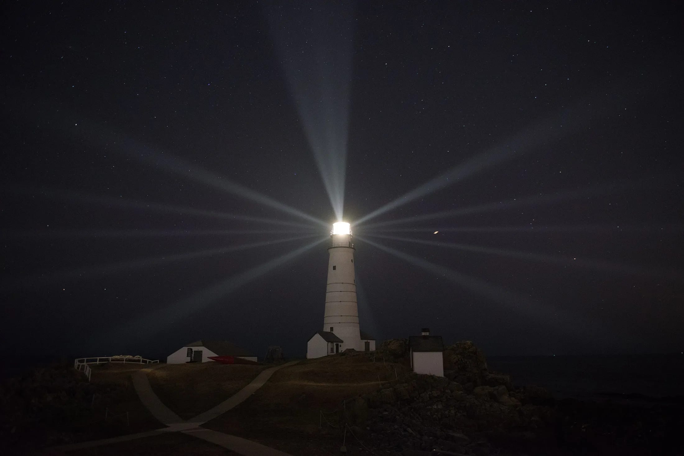 A lighthouse at night, its beams sweeping out across a dark sky.