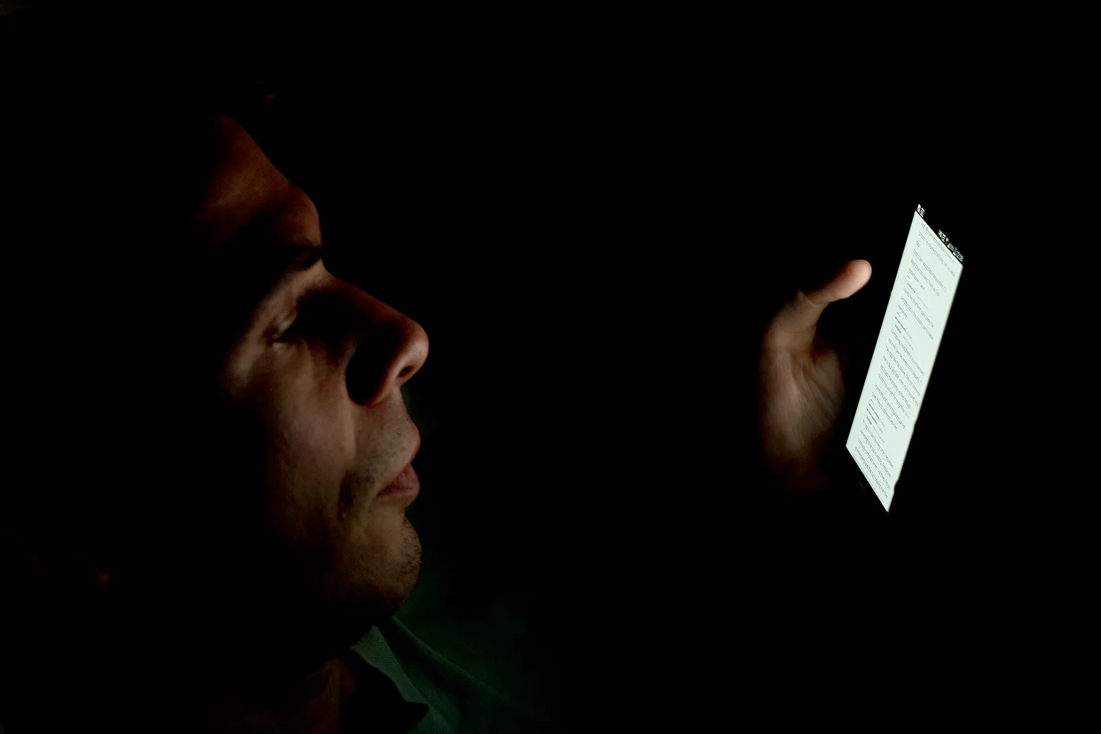 A face in the dark, lit only by the phone the person is reading.